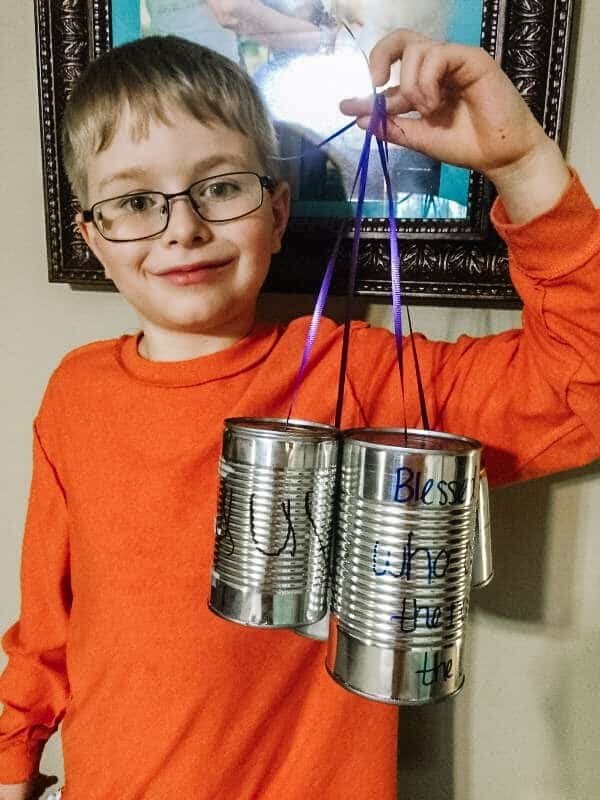 Boy hold 3 tin cans attached to purple ribbon. The cans have Bible verses on them. | 6 Special Christian Easter Activities for Families